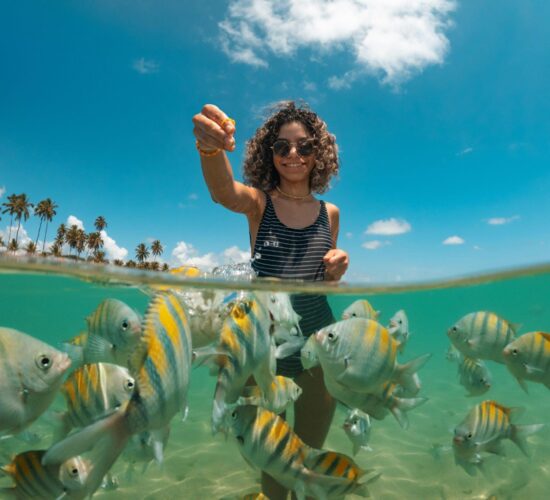 Girl feeding colorful fish in clear waters of Nassau Bahamas.