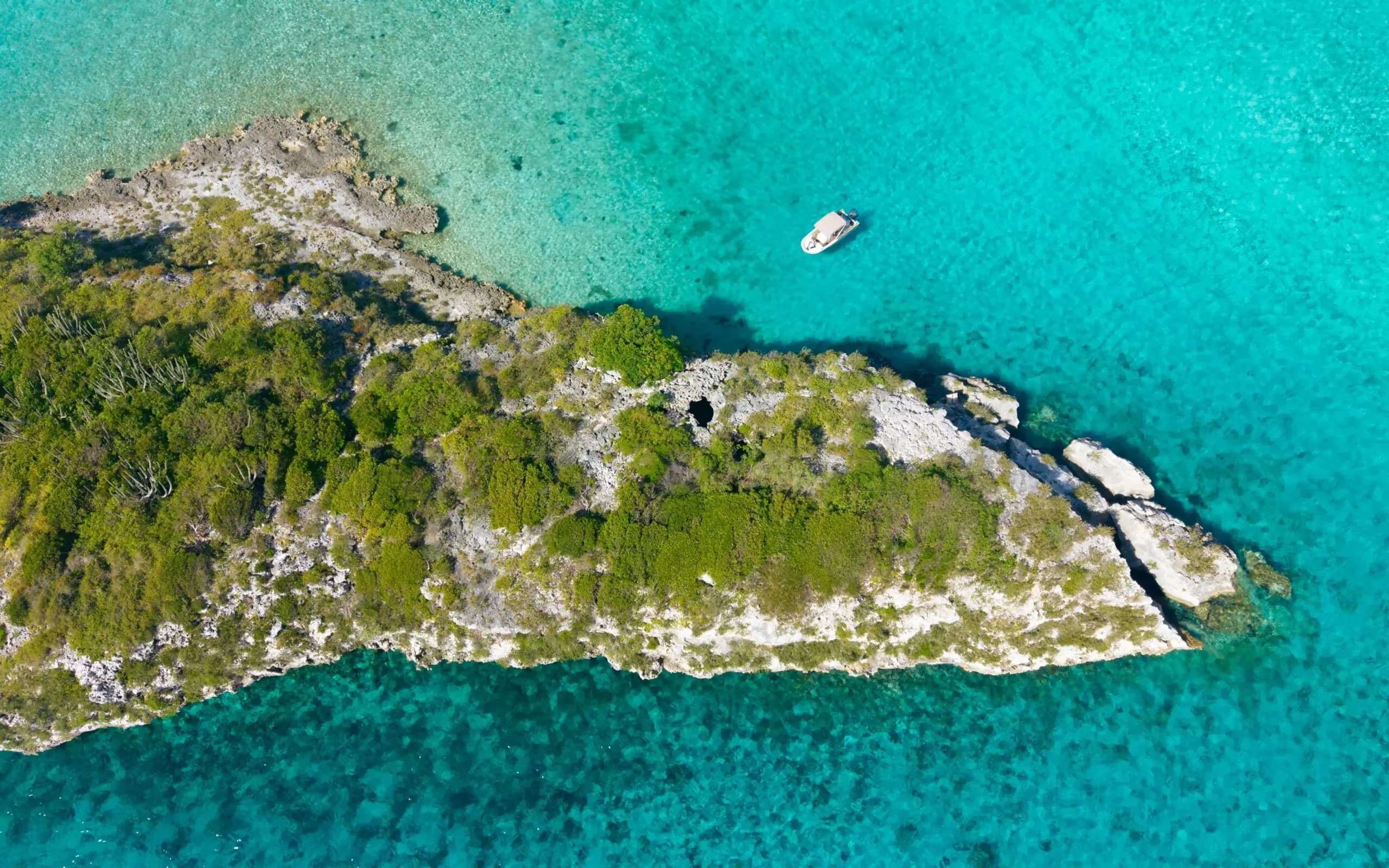 Aerial view of a private boat near secluded rocky shoreline and turquoise water at 007 Thunder Ball Grotto Bahamas