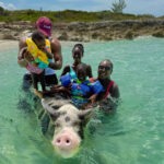 Smiling guest holding piglet on Rose Island Bahamas beach